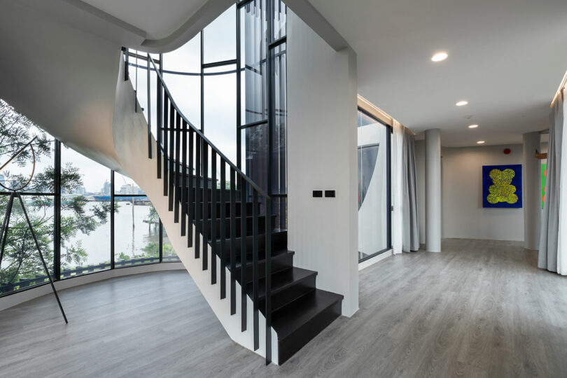 Modern interior featuring a black spiral staircase, large floor-to-ceiling windows with a view of the outdoors, and contemporary decor with abstract wall art.