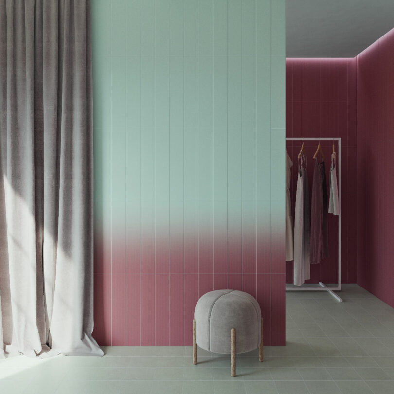 A modern room with a gradient pink-to-green wall, grey curtains, a small round grey ottoman, and a clothing rack with various garments hanging.