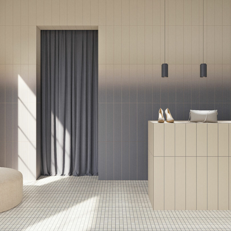 Minimalist interior with a tiled floor, a light beige counter holding a pair of shoes and a small bag, gray curtains, pendant lights, and sunlight streaming through a window.