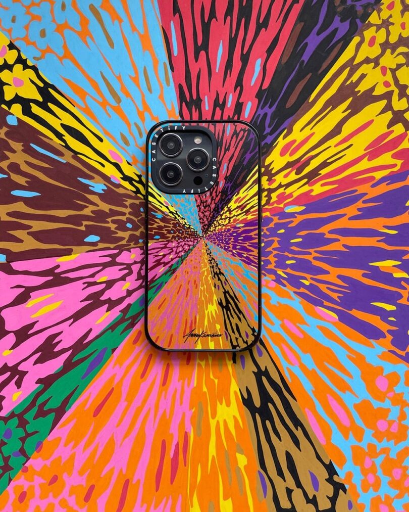 A smartphone with a black case and colorful abstract design is placed on a similarly vibrant, multicolored abstract background