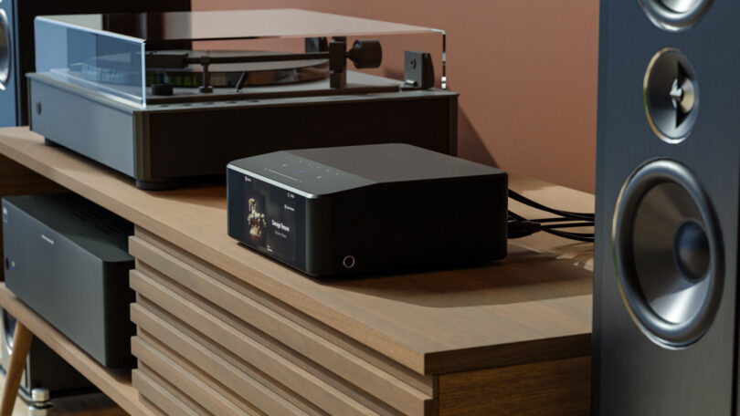 Audio equipment including a turntable, media player, and speaker is arranged on a wooden shelf.