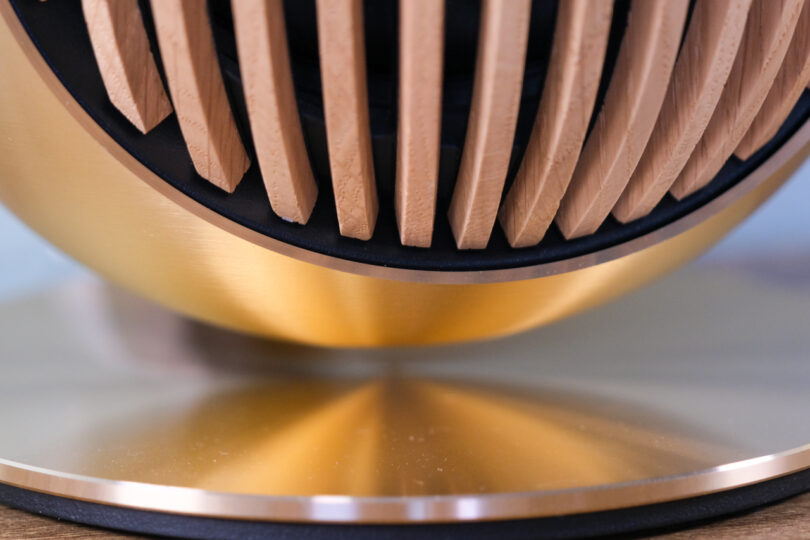 Close-up of a modern, abstract sculpture featuring vertical wooden slats in the upper section and a smooth, reflective golden base.