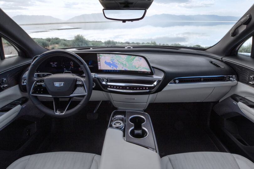 Interior view of a modern car featuring a digital dashboard with a GPS map displayed, a multifunction steering wheel, and a central console with cup holders, against a backdrop of a lake and mountains.