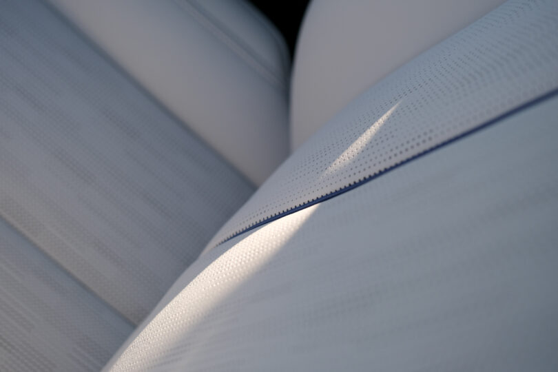 Close-up of light-colored, perforated leather car seats with a shadow cast on them.