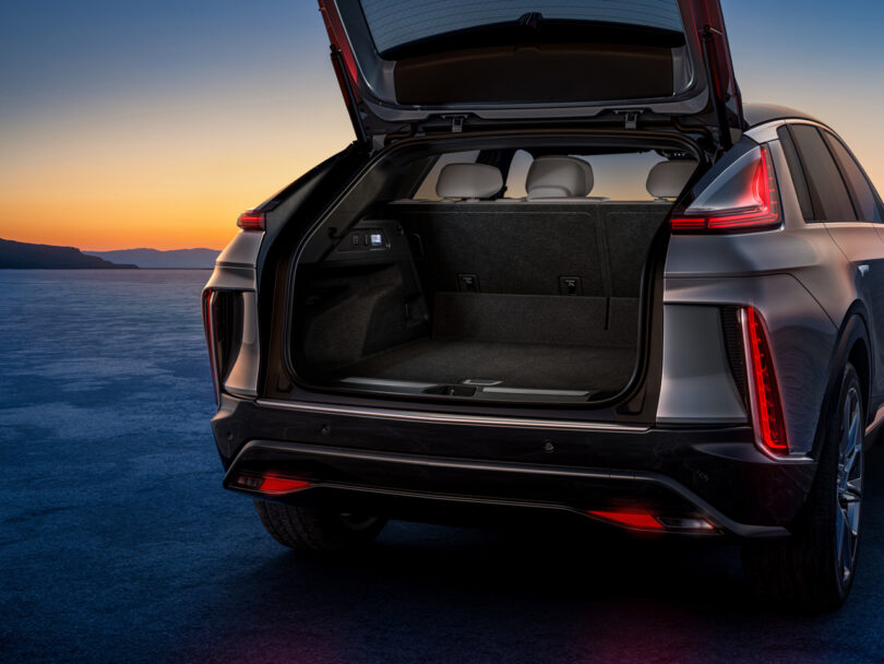 Open trunk of a modern SUV shown at sunset, highlighting spacious cargo area with rear seats visible. Rear lights illuminated and tailgate fully raised.