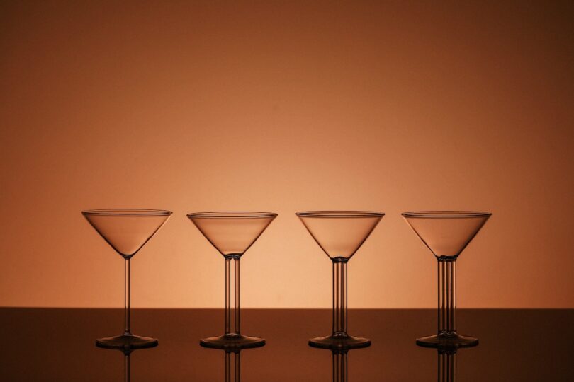 Four empty martini glasses are aligned in a row against a warm, orange background