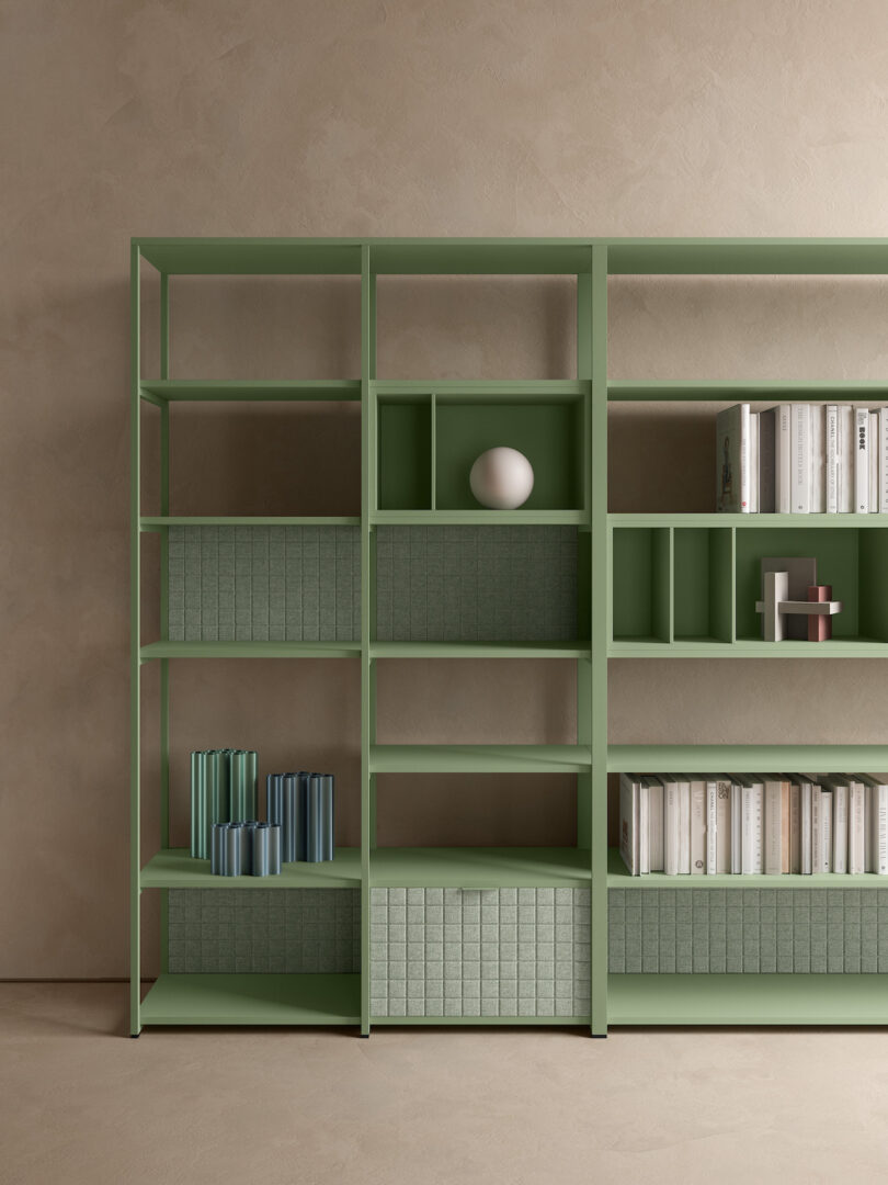 A minimalist green bookshelf against a beige wall, holding an assortment of books and a single decorative white sphere