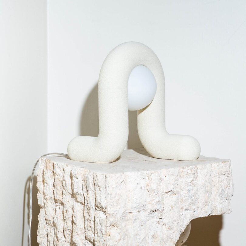 A unique U-shaped light fixture with a white bulb is placed on a rough, textured stone pedestal