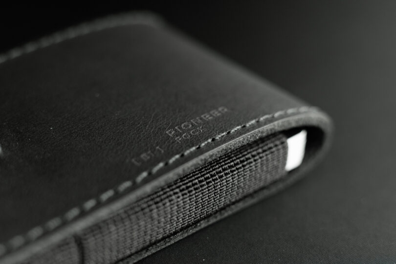 Close-up of a black leather wallet with visible stitching and a fabric interior. The word "Pioneer" is embossed on the leather.