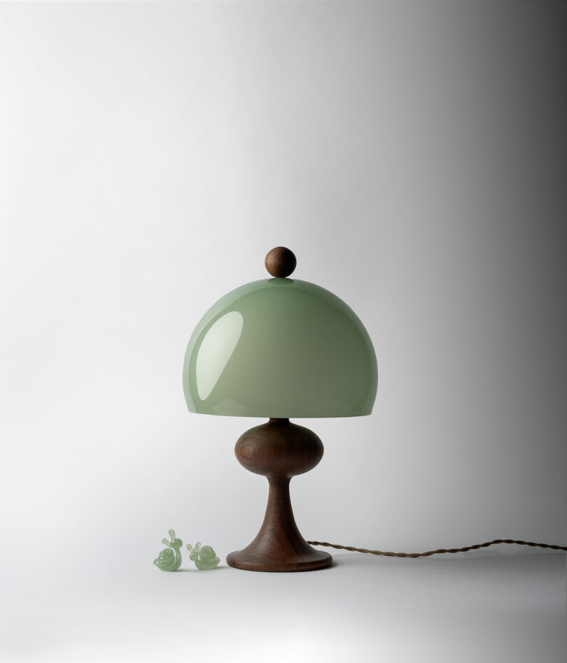 A table lamp with a green dome-shaped shade and wooden base. Two small green snail figurines are placed beside the lamp