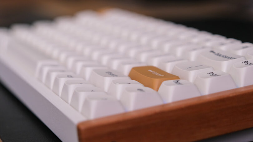 Close-up of a white mechanical keyboard with a wooden frame and a single brown keycap.