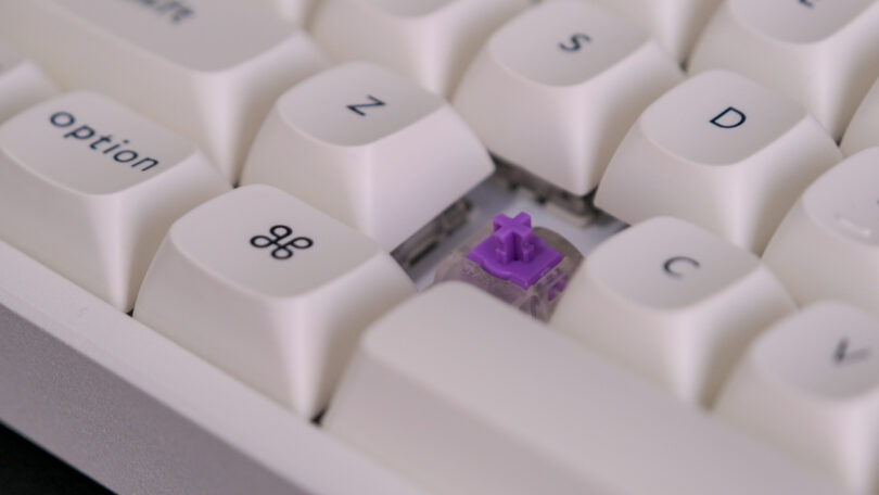 Close-up of a mechanical keyboard showing a missing keycap and exposed purple switch among white keycaps.