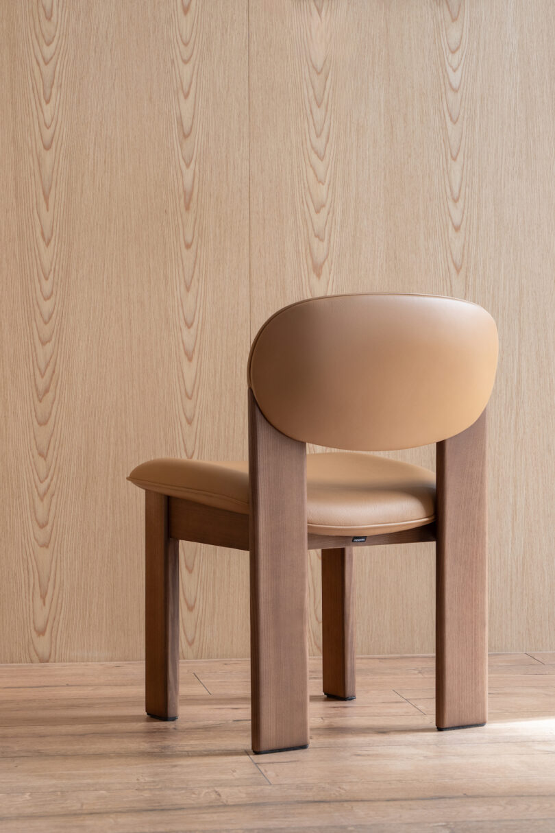 A wooden chair with a brown leather seat and backrest is placed in front of a wooden wall