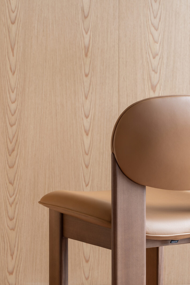 A brown leather cushioned chair with a wooden frame is positioned in front of a wooden panel wall featuring a natural grain pattern