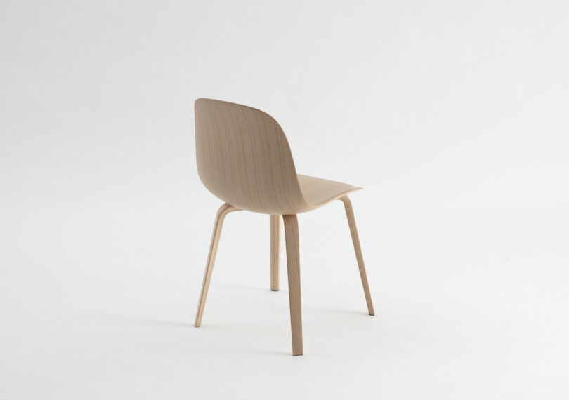 A minimalist wooden chair with a curved backrest and four legs, set against a white background