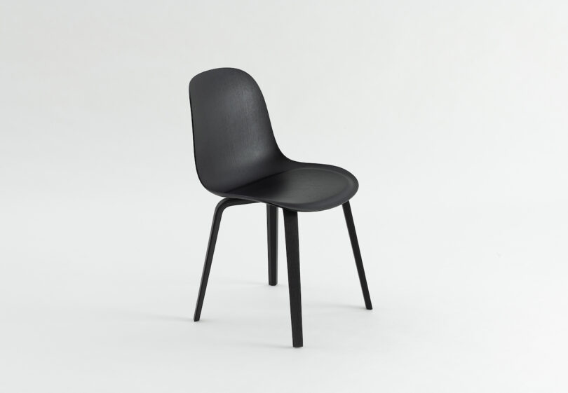 A black, modern, four-legged chair with a curved seat and backrest is centered on a plain white background