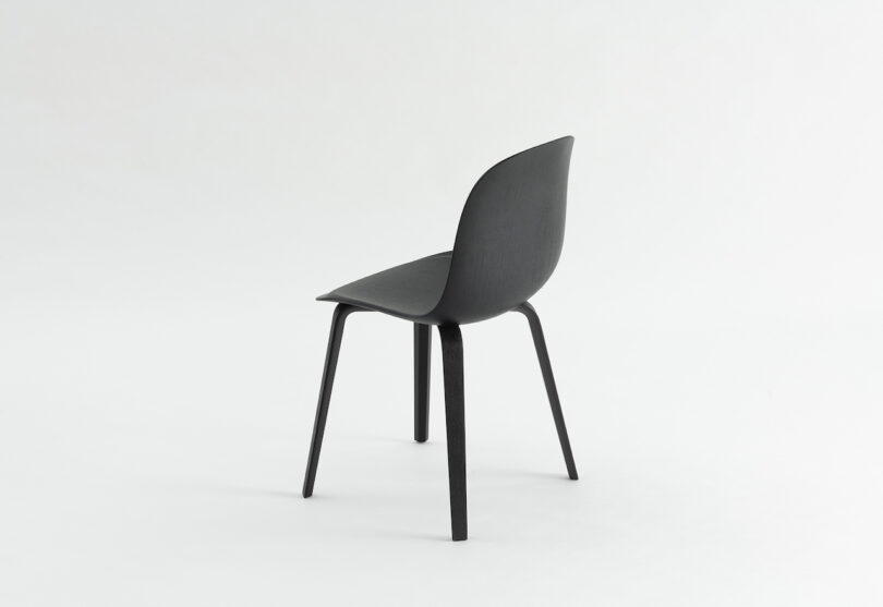 A modern black chair with a curved backrest and seat, supported by four angled legs, shown against a plain white background