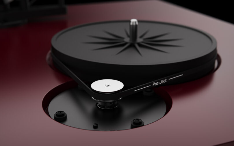 Close-up of a modern turntable with a black platter and tonearm against a dark contrasting background.