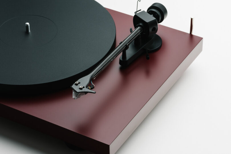 Close-up of a turntable with a black tonearm and stylus positioned on a sleek, red base. The turntable platter is empty and ready for a vinyl record.