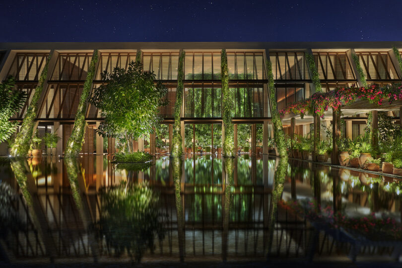 A night view of The Riviera Maya EDITION at Kanai with timber-clad exterior walls and lush greenery reflected in a tranquil pool