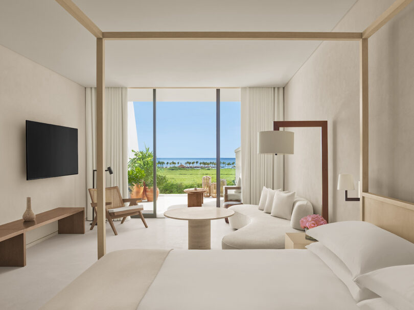 A minimalist guest room at The Riviera Maya EDITION, featuring neutral tones, a four-poster bed, and a view of the ocean