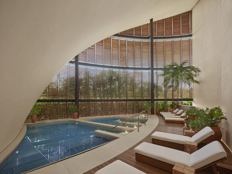 An indoor pool at The Riviera Maya EDITION spa, surrounded by wooden shutters and greenery