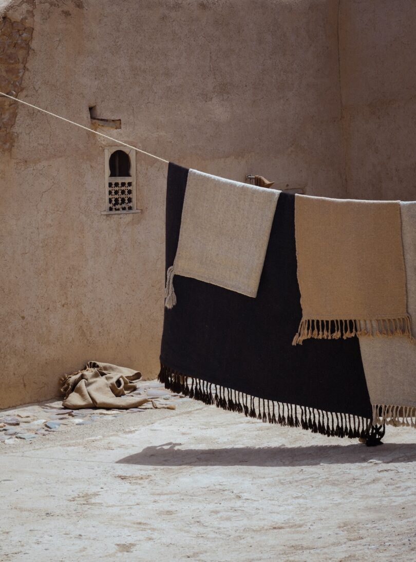 A collection of undyed Terrain rugs hanging on a clothesline against a textured wall