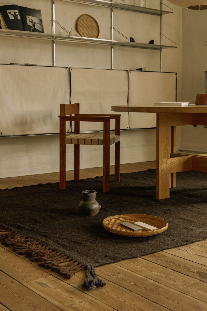 A minimalist interior featuring a dark-toned Beni rug with simple wooden furniture and a few curated objects