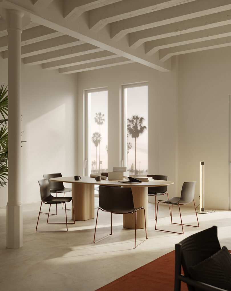 A modern office space with a round Ghia Table surrounded by black chairs, large windows showing a view of palm trees, and minimalistic decor with exposed ceiling beams and a potted plant.