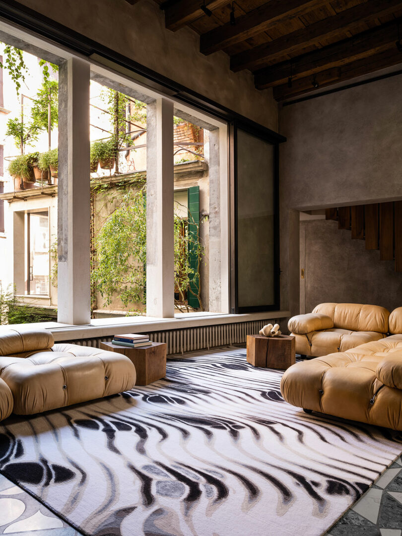 A living room with large windows, beige sofas, a patterned rug, and wooden elements showcases a Dale Chihuly piece, featuring a view of a garden outside.