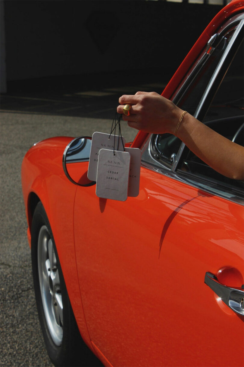 A person extends their hand out of an orange car window, much like Kate Rohrer might in her own adventures, holding three hanging air fresheners.