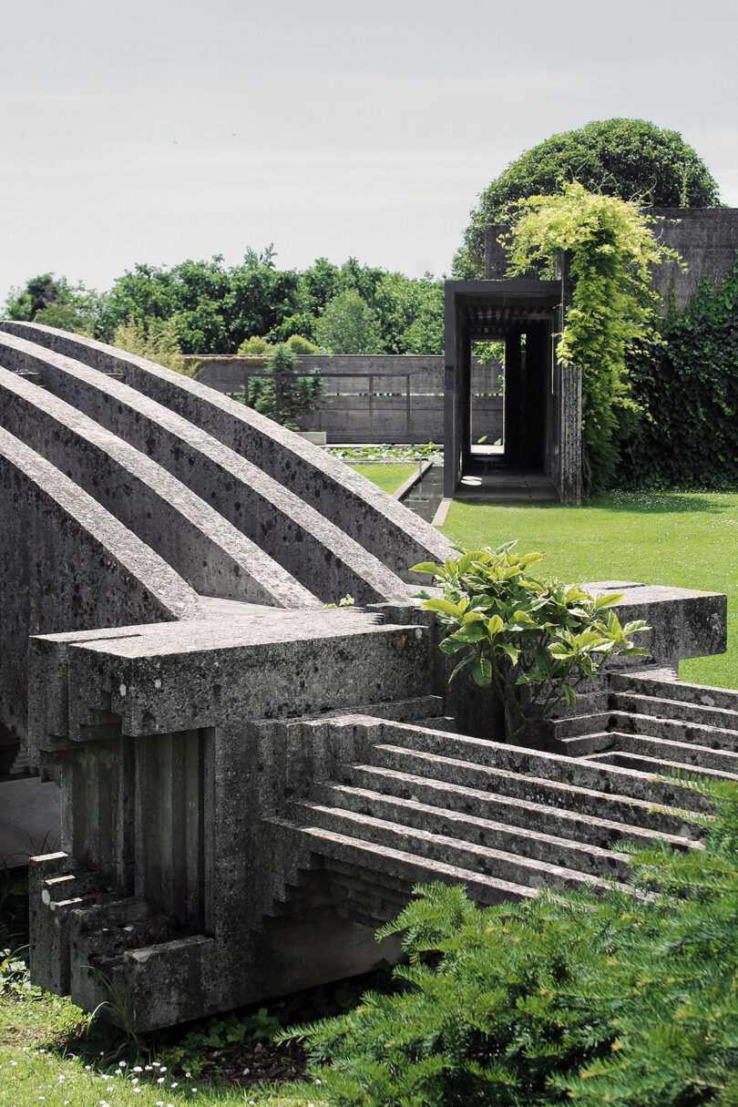 Concrete, stylized arches and walkways are part of a modern architectural structure with greenery and trees in the background.