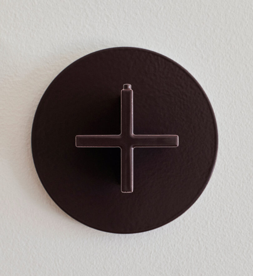 A close-up image of a round, dark brown wall-mounted knob with a cross-shaped handle.