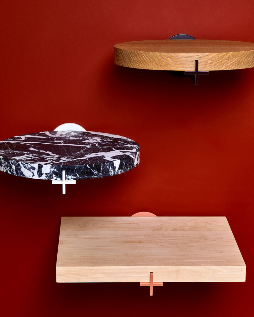 Three wall-mounted shelves against a red background: a round wooden shelf, a round black and white marble shelf, and a rectangular light wood shelf.