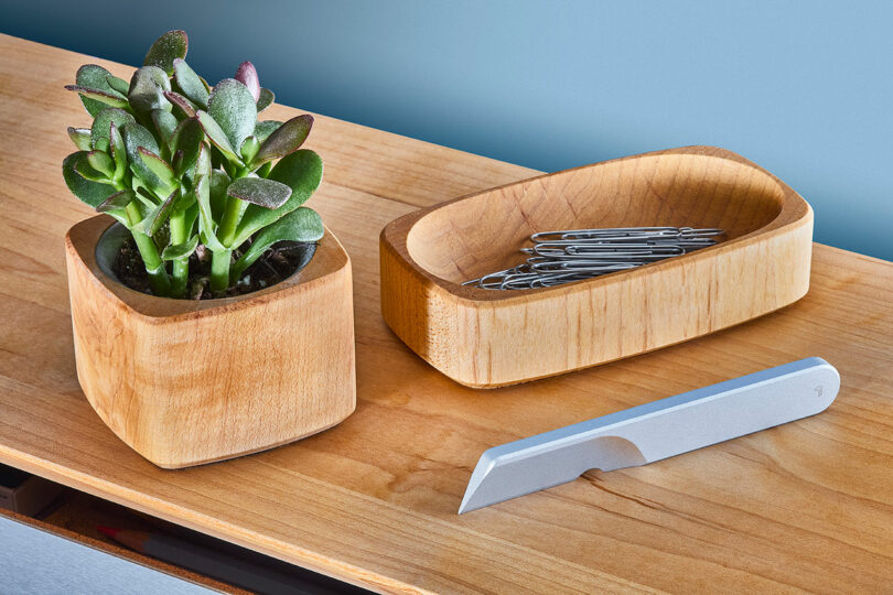 A small potted succulent, a wooden bowl with paper clips, and a Task Knife from Grovemade rest on a wooden surface.