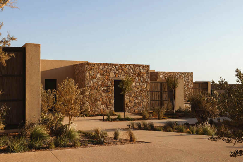 A modern, single-story building with stone and stucco exterior walls, surrounded by a minimalist landscaped garden featuring various shrubs and grasses.