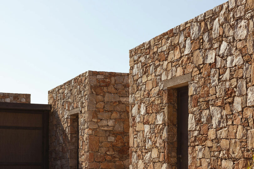 Exterior view of a modern building featuring stone walls with large rectangular windows and a wooden door under a clear sky.