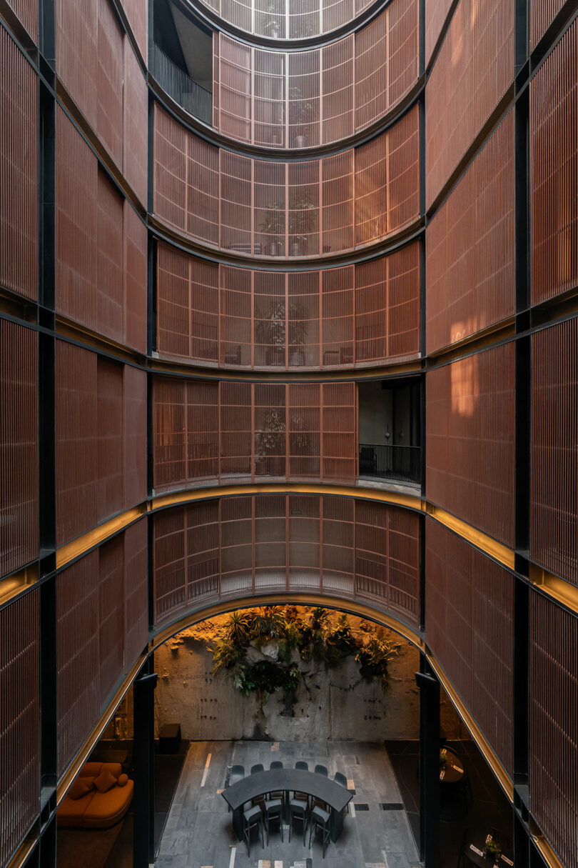 A high, cylindrical atrium at Hotel Volga with multiple floors features a circular seating area and lush greenery at the base. Sunlight streams down, highlighting the modern architecture and vertical lines.