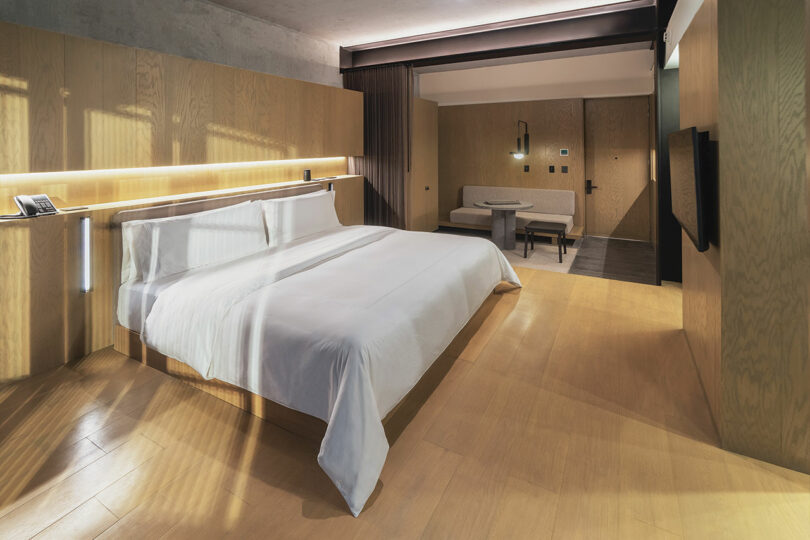 Modern Hotel Volga room featuring wooden floors and walls, a large bed, a flat-screen TV on the wall, a cozy sitting area with a table, and minimalist decor.