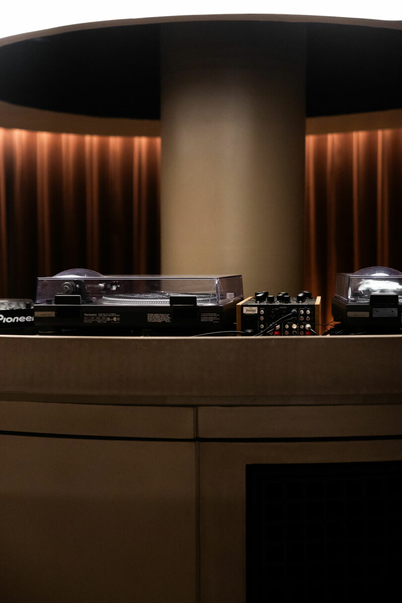 A DJ setup featuring turntables and audio equipment on a sleek countertop with a backdrop of vertical curtains.