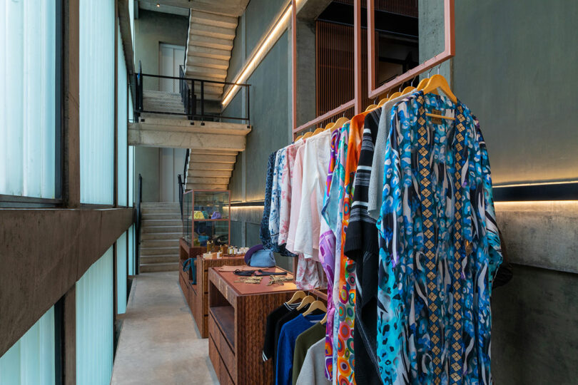 A modern clothing store with colorful garments hanging on wooden racks, glass cases displaying accessories, and a concrete staircase.