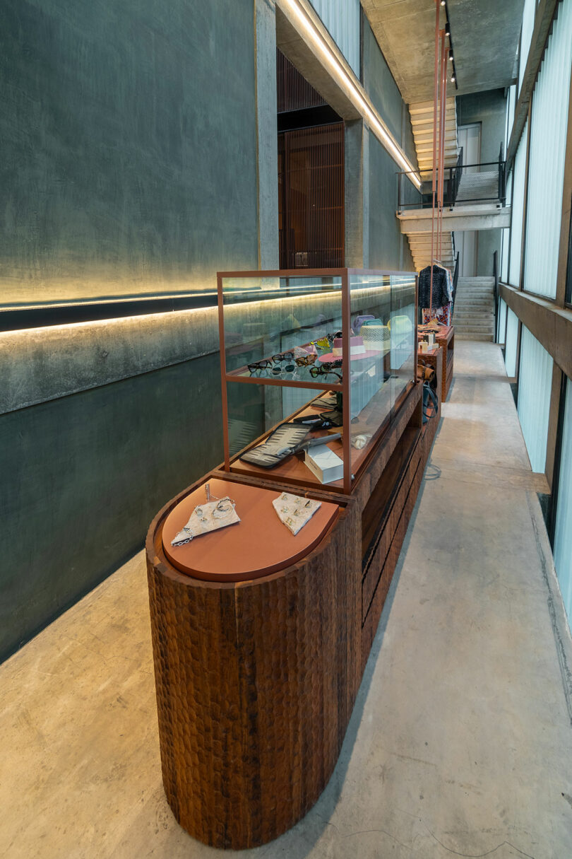 A modern retail display featuring a wooden and glass showcase filled with various items, set in an industrial-style store complete with concrete walls, high ceilings, and a staircase in the background.