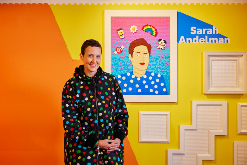 A person stands in front of a brightly colored portrait with a pixelated frame on a wall. The background features vibrant orange and yellow hues, with the name "Sarah Andelman" displayed to the right.