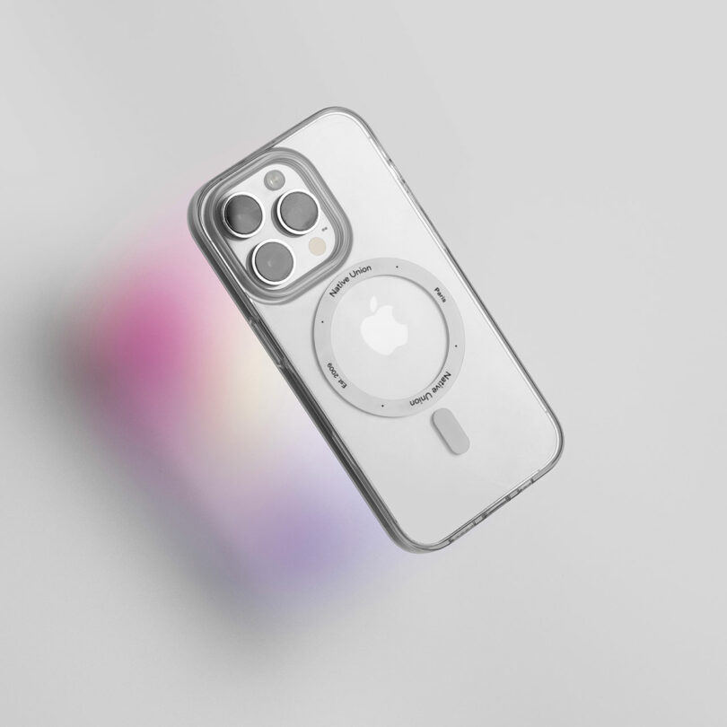 Clear phone case with a circular MagSafe ring on the back, protecting an iPhone with a triple camera setup. The image, featuring Native Union's design aesthetics, showcases a gradient light cast in the background.