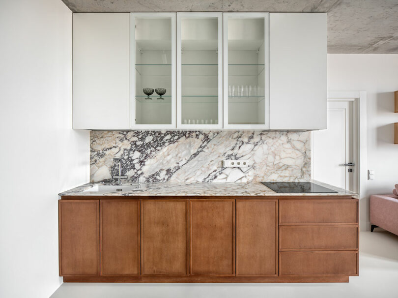 Modern kitchen with a brown lower cabinet, marble backsplash and countertop, and a white upper cabinet with glass doors. Equipped with a sink on the left and an electric cooktop on the right.