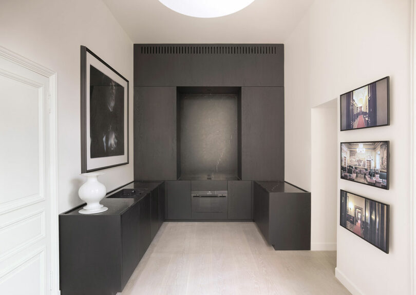 Minimalist room with modern black built-in cabinets, light wood flooring, and framed artwork on the walls. Bright lighting from a circular ceiling fixture illuminates the space.