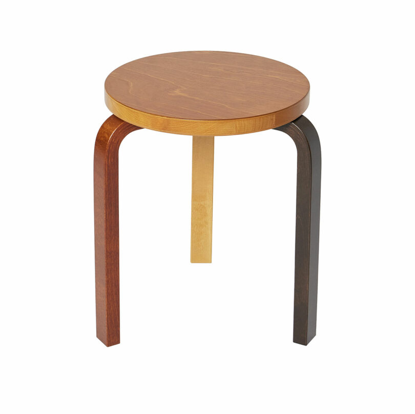 Stool 60 by Alvar Aalto with a round top and three legs, each leg painted in a different color: dark brown, light beige, and black.