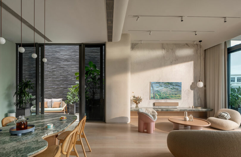 Modern living and dining area featuring minimalist decor, a marble dining table, wooden chairs, green plants, and a cozy seating space with round coffee table and neutral-toned furniture.