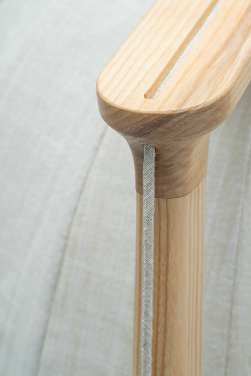 Close-up of the Shanti Chair's wooden armrest with a fabric cord detail. The armrest features a slot through which a light-colored cord passes, highlighting the craftsmanship of this elegant furniture piece.