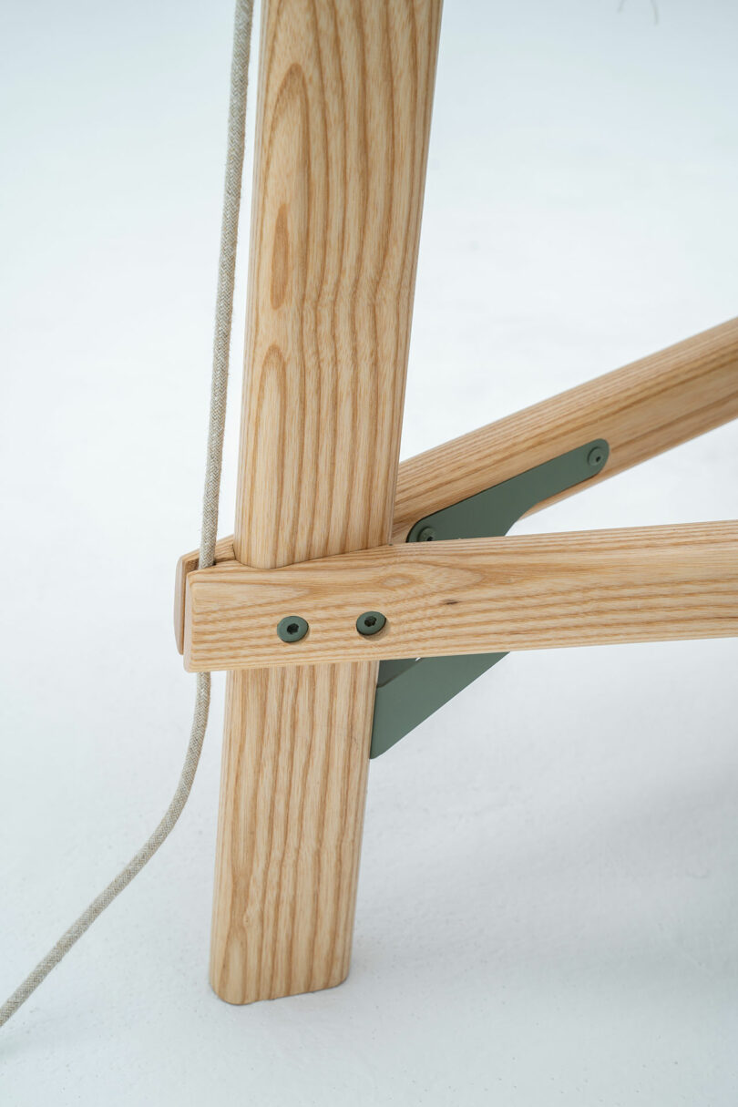 Close-up of a Shanti Chair's wooden leg with a support bracket and two screws securing it. A white cord is looped around the leg.